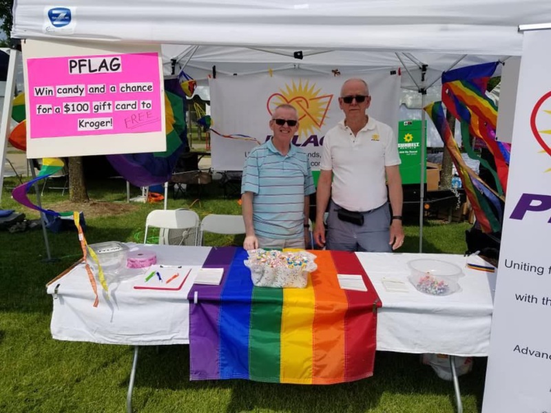 Two men standing in a booth at a pride festival.