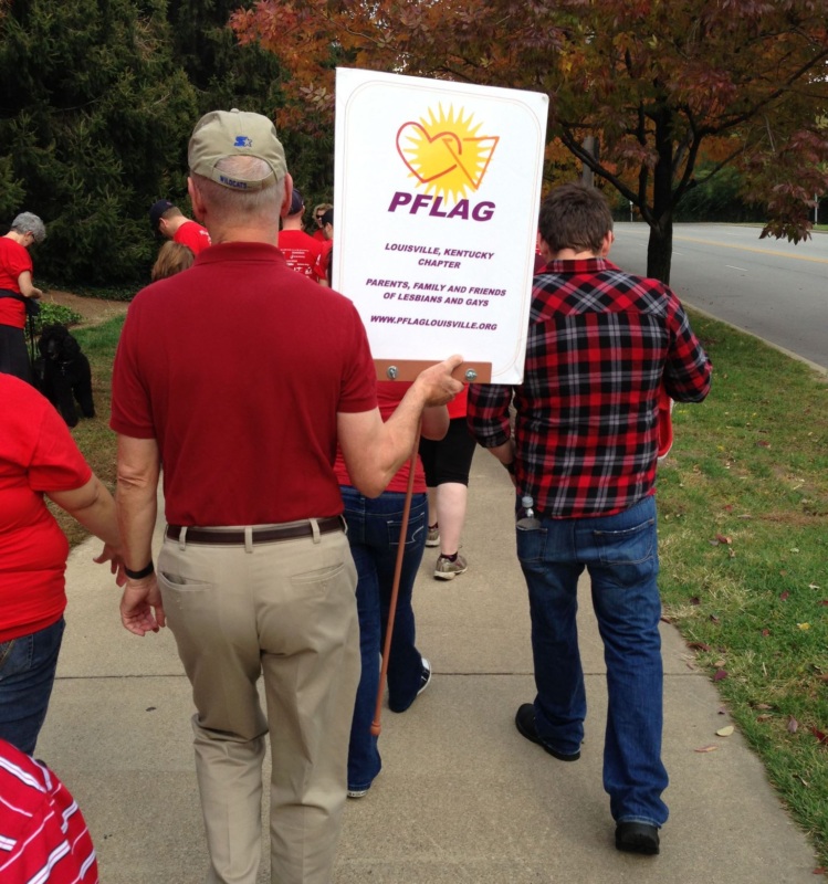 Man walking down sidewalk with PFLAG sign.